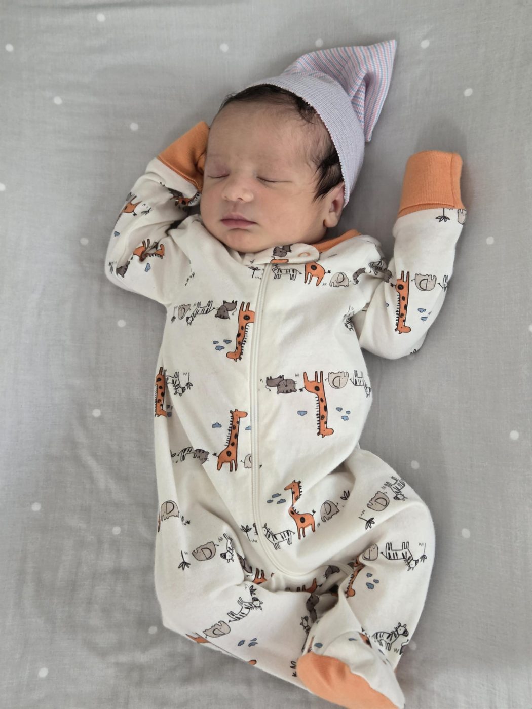 Faris asleep in a giraffe-print sleeper and striped newborn hat